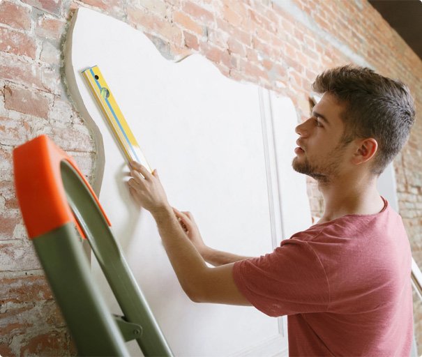Handyman measuring and aligning drywall on a brick wall using a spirit level.